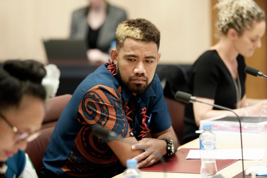 A man leans on a table in a parliamentary committee room