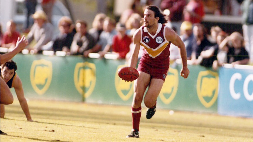 Man with dark hair playing Australian Football.