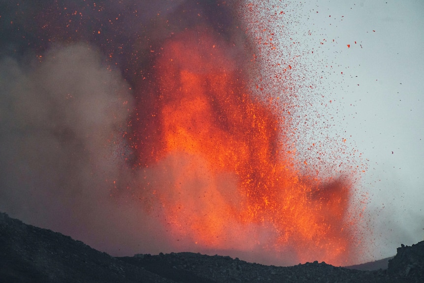 A red burst of lava erupts from a crater.