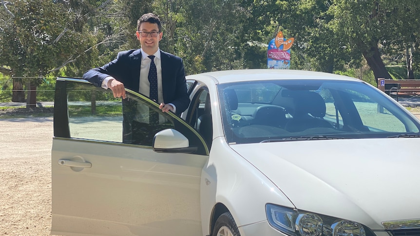 A man standing inside the open front door of a car