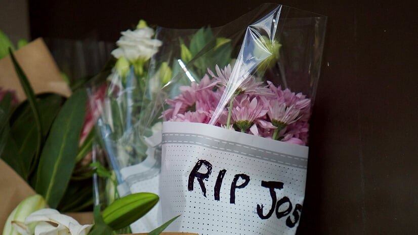 A bouquet of pink flowers wrapped in paper reading 'RIP Josh' is laid amongst a row of tributes.