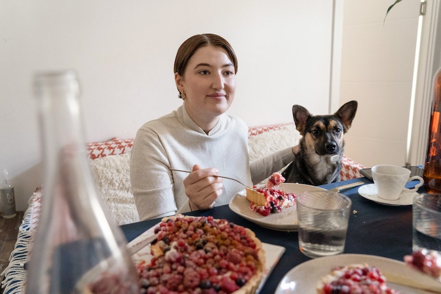 一个女人和一条狗并排坐在沙发上，女人正在吃馅饼盘，狗在打哈欠