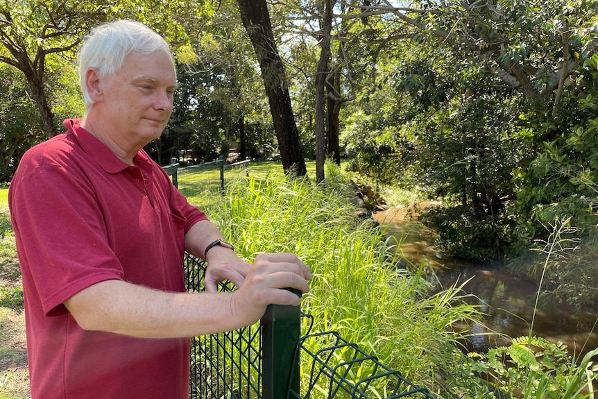 An elderly man looks into a creek.