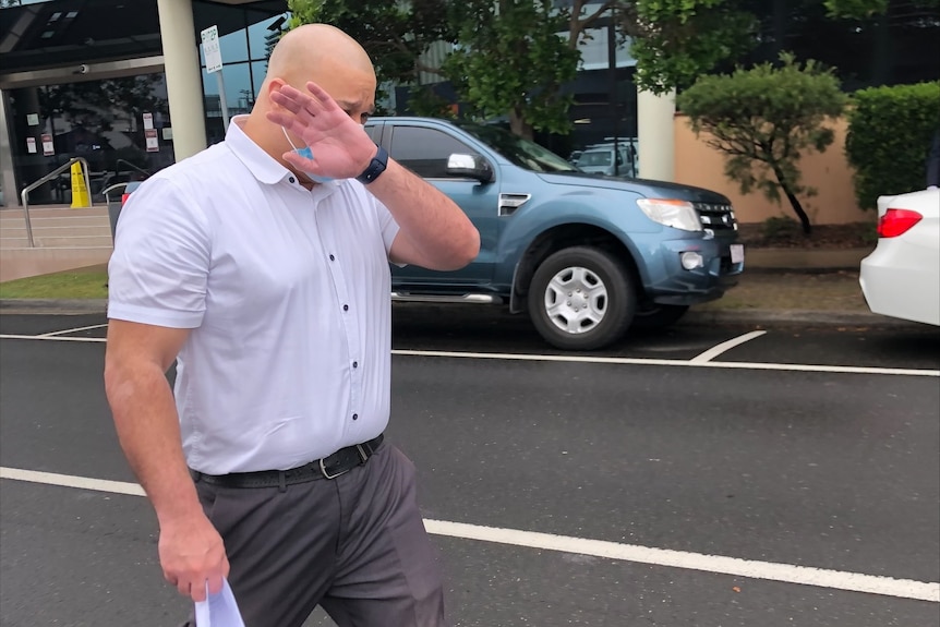 bald man with white button up t-shirt covers his face with hand as he leaves court