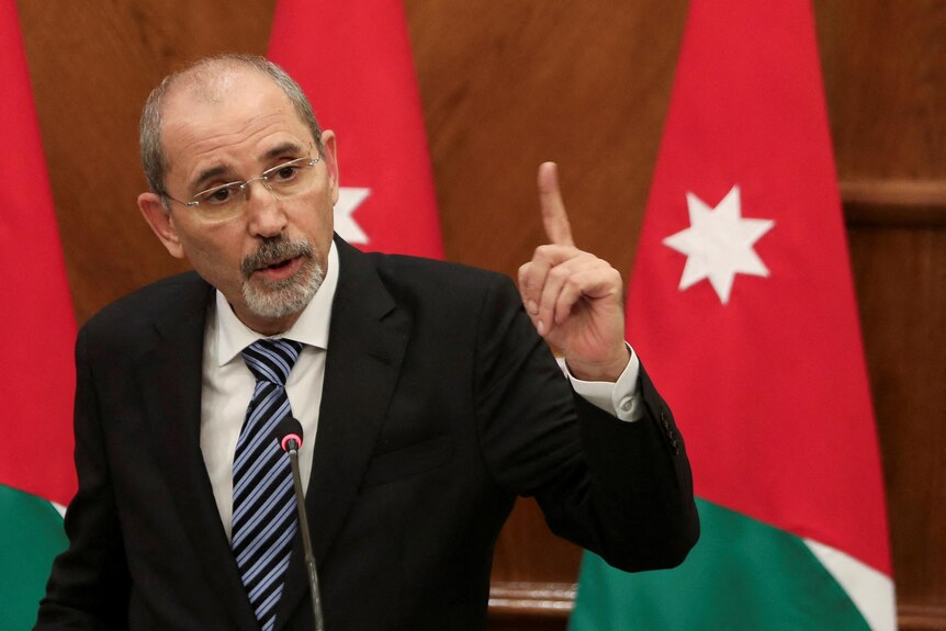 Jordan's Foreign Minister Ayman Safadi wearing a suit speaking at a press conference with his hand raised.
