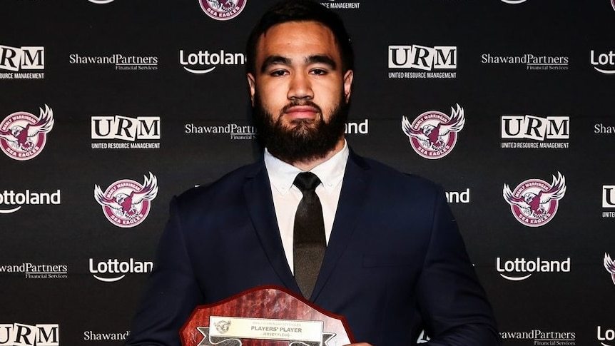 A Manly rugby league players stands holding an award.
