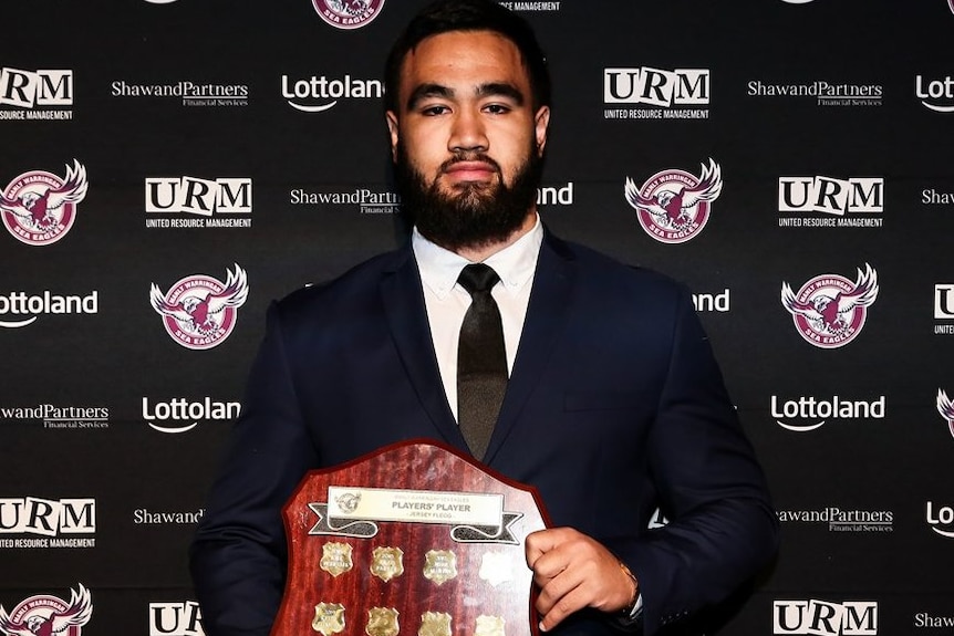 A Manly rugby league players stands holding an award.