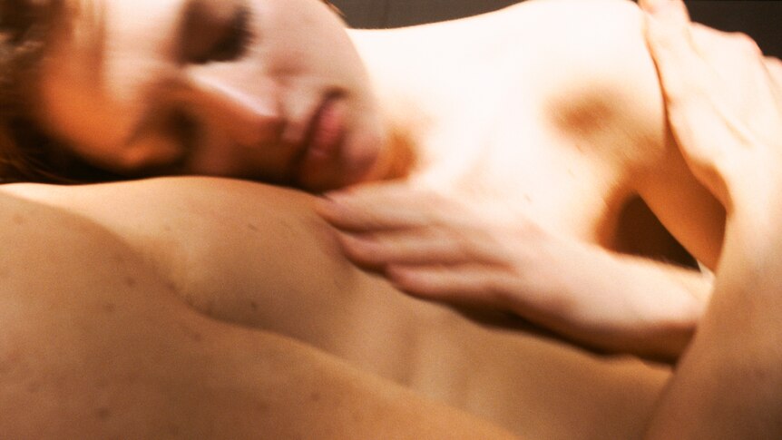 A blurred image of a woman's face and hand lying on the torso of a naked man