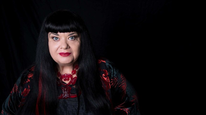 Lynette Wallworth with dark hair with a fringe, against a black background. She is wearing a red necklace