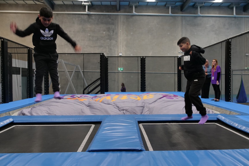 Two kids in black hoodies play on trampolines