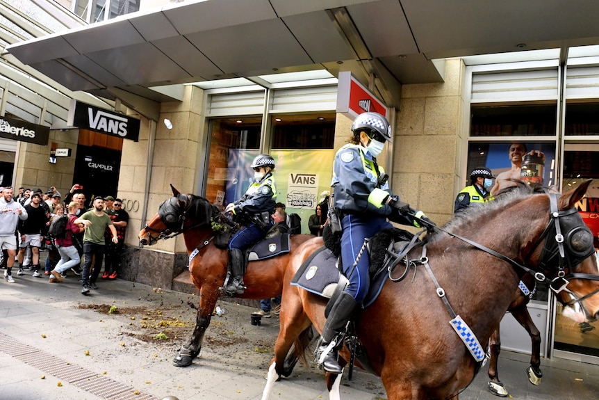 uniformed police wearing face masks on horseback are confronted by a group of anti-lockdown protesters in Sydney