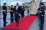 Australia Prime Minister Scott Morrison walks on a red carpet flanked by military personnel as he leaves a plane.