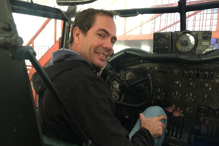 A man sitting in the cockpit of a Lancaster bomber on an airfield.