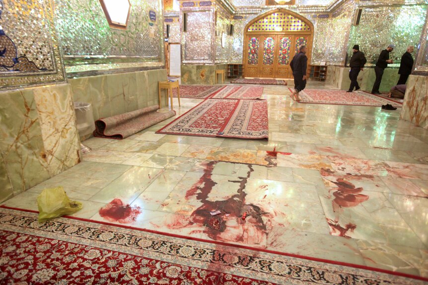 Blood is seen on the ground as men walk in the background of the Shah Cheragh shrine.