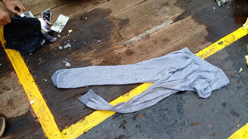 Wet tracksuit pants lie on a boat's deck with a damage mobile phone case and handbag