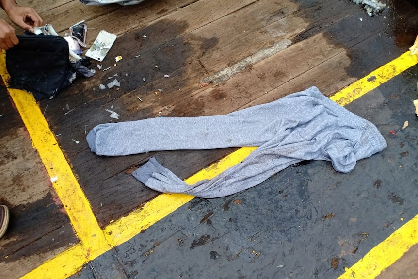 Wet tracksuit pants lie on a boat's deck with a damage mobile phone case and handbag