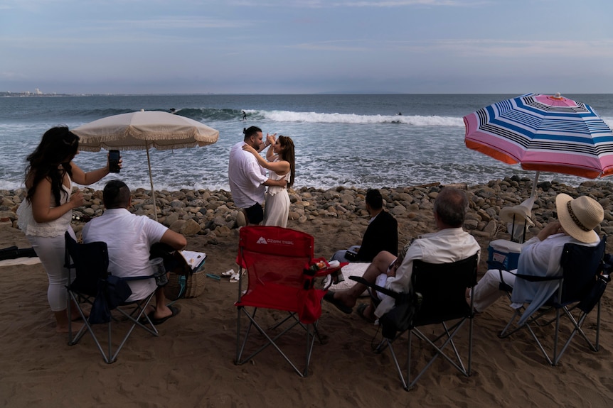 Couple dance in front of family on a beach in Malibu.