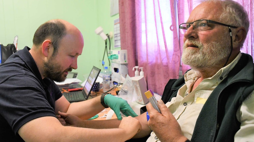 A doctor takes blood from an older man at a clinic