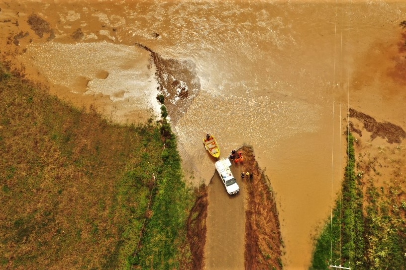 A car and boat on the bank of brown floodwaters.
