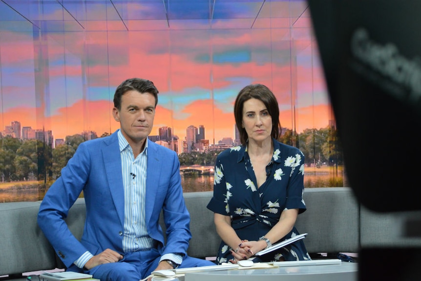 Rowland and Trioli looking at TV camera with serious looks on their faces.