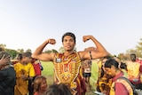 A Halls Creek Hawks player flexes his muscles in front of a group of people at Kununurra Oval. 