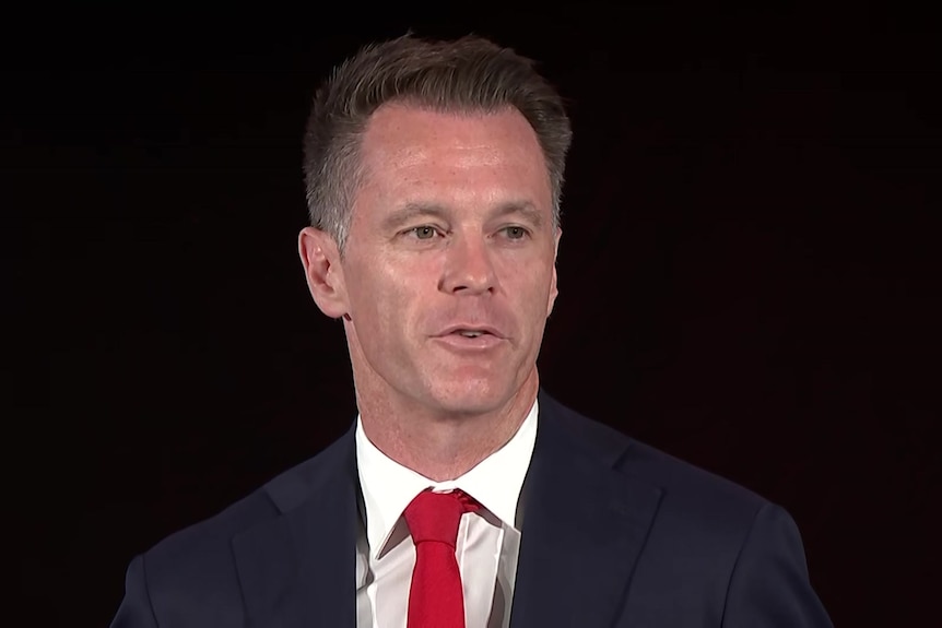 a man wearing a suit and tie talking to a room full of people