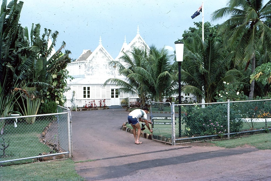 An archival photo of a man opening a fence in front of Government House.