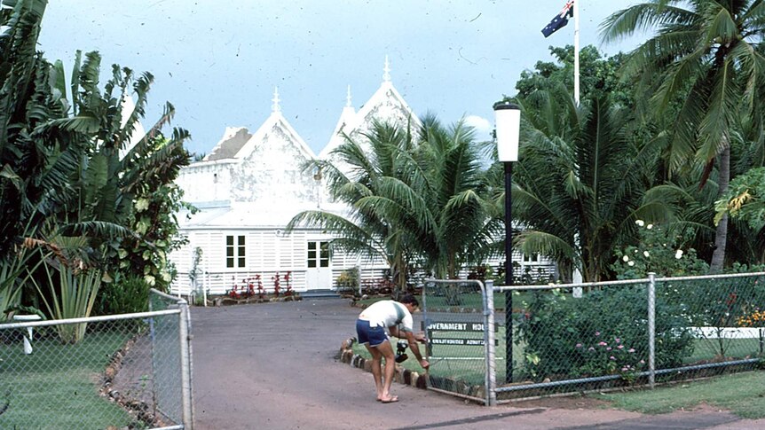 An archival photo of a man opening a fence in front of Government House.