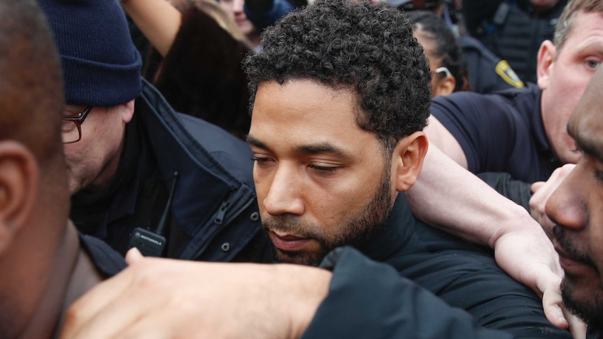 Jussie Smollett stands in a crowd of people with one hand on a man in front of him as leaves Cook County Jail.