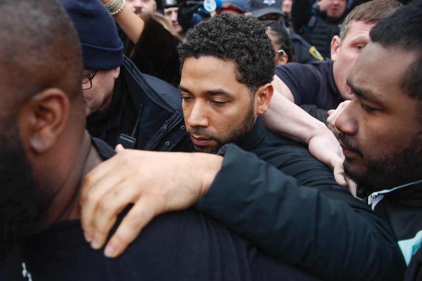Jussie Smollett stands in a crowd of people with one hand on a man in front of him as leaves Cook County Jail.