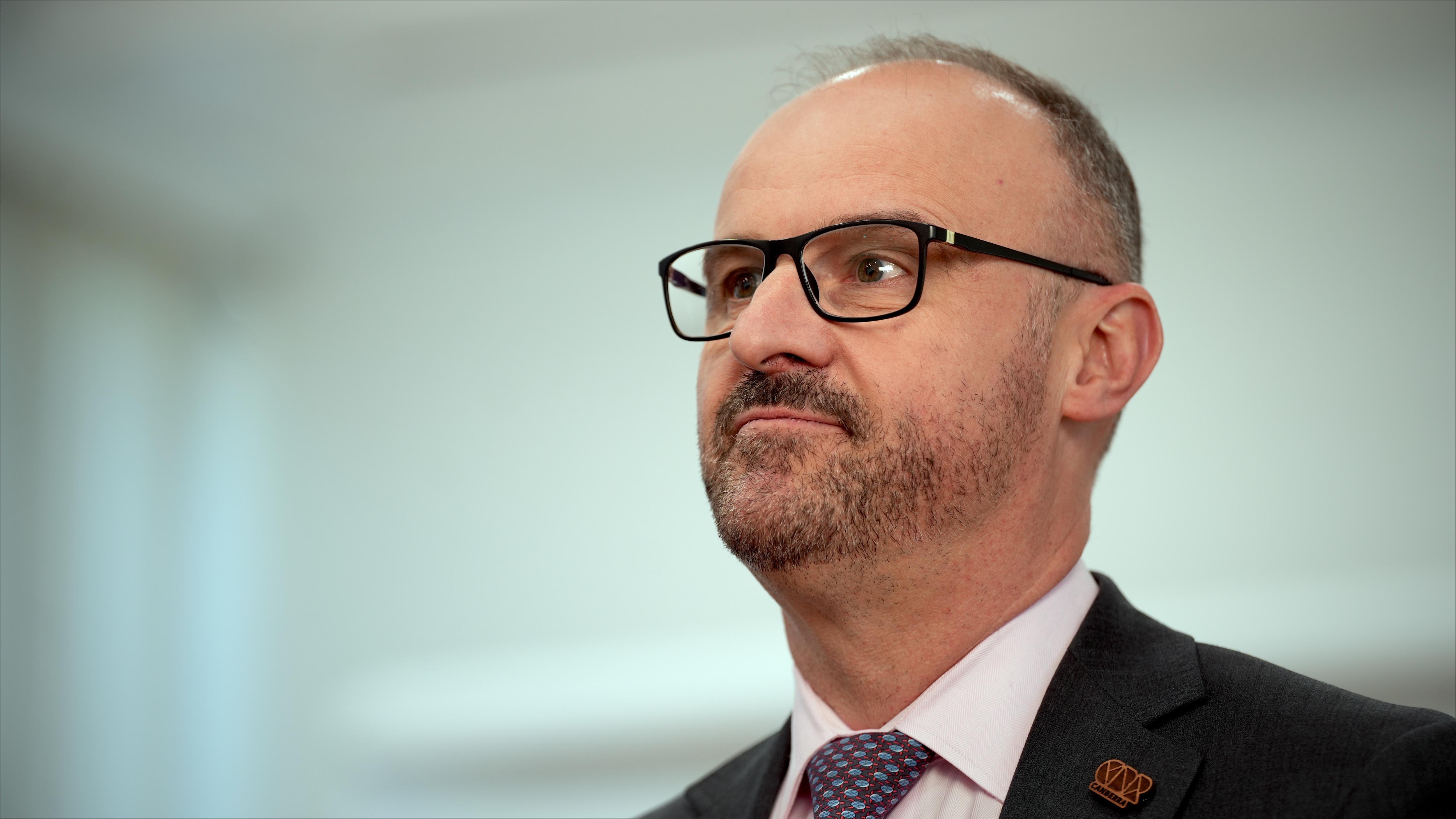 A man stands wearing glasses and listening.