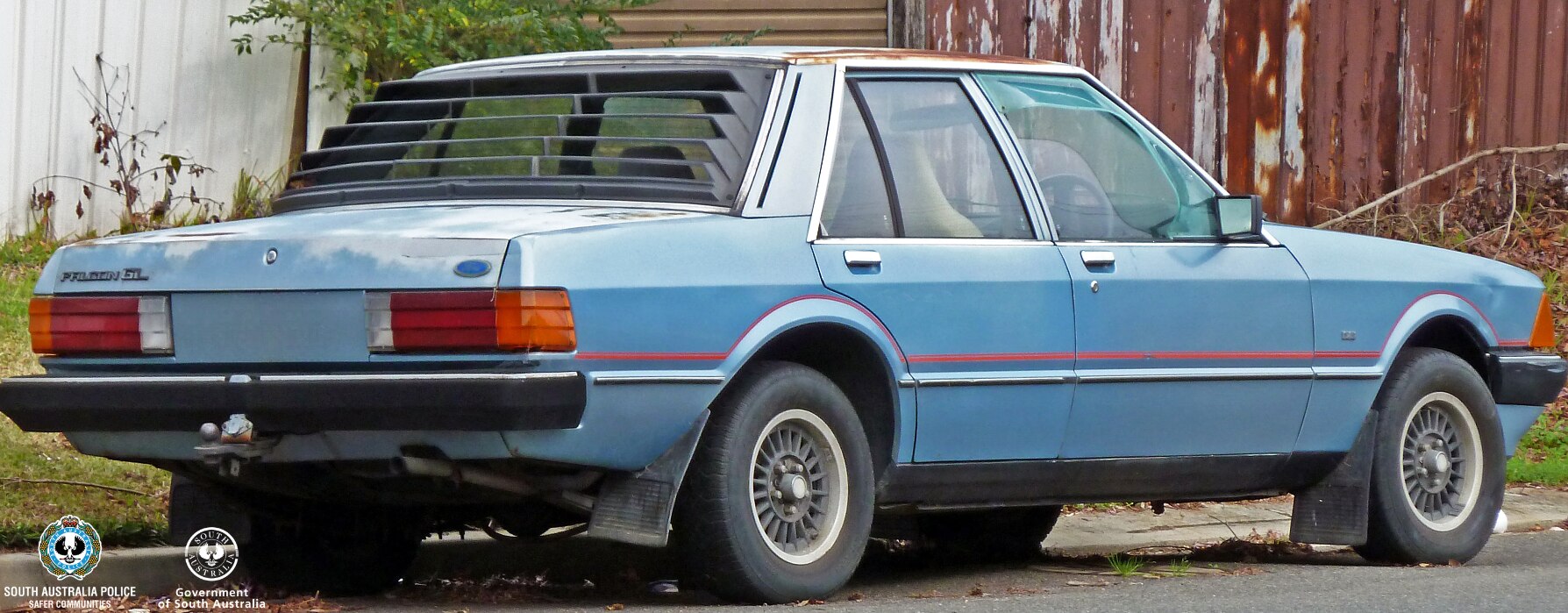 A blue sedan with red line across the middle packed on a street next to a rusty fence