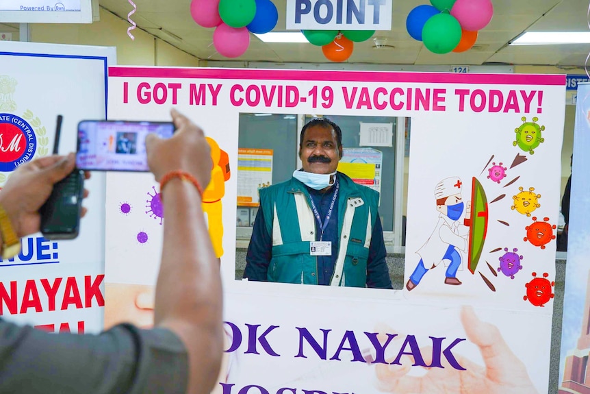 A man posing for a photo above a sign reading 'I got my COVID-19 vaccine today!'