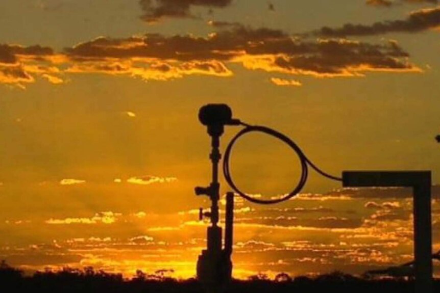 A coal seam gas well silhouetted against a golden sky