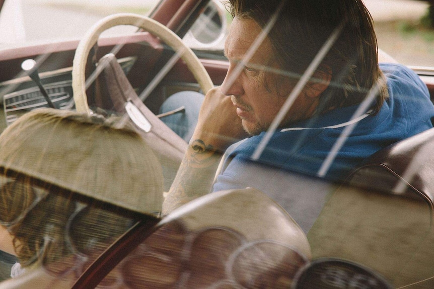 A man in an old car leans over to his son.