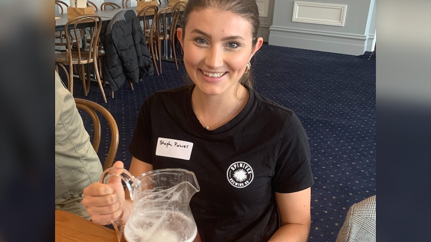 Steph Power holds a jug of beer next to a glass ready to fill it up with beer.