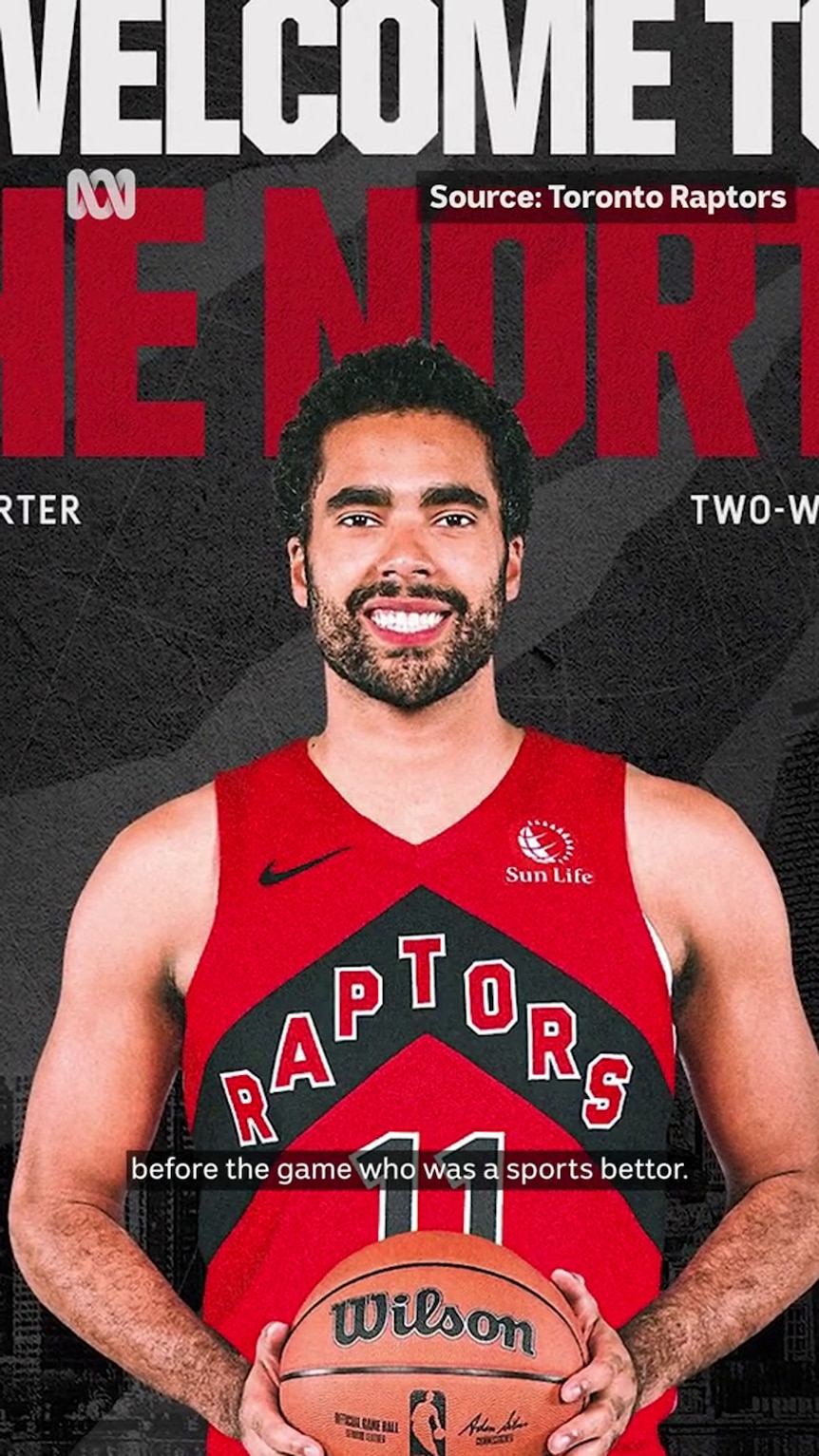 A man in a red and black Raptors singlet numbered 11 smiles while holding a Wilson basketball