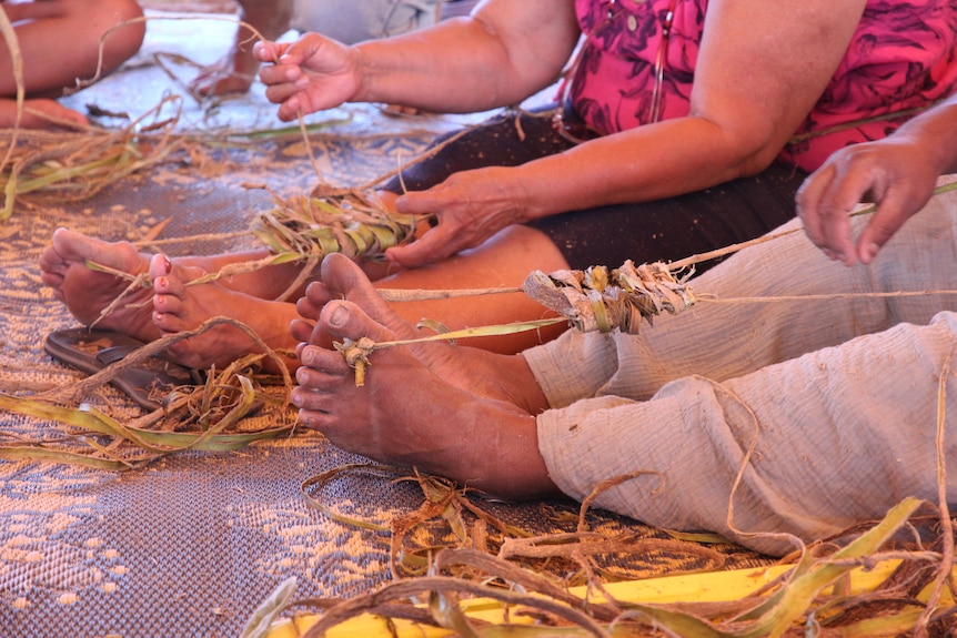 Hands weaving pieces of rough tree calved pieces of rope around feet.