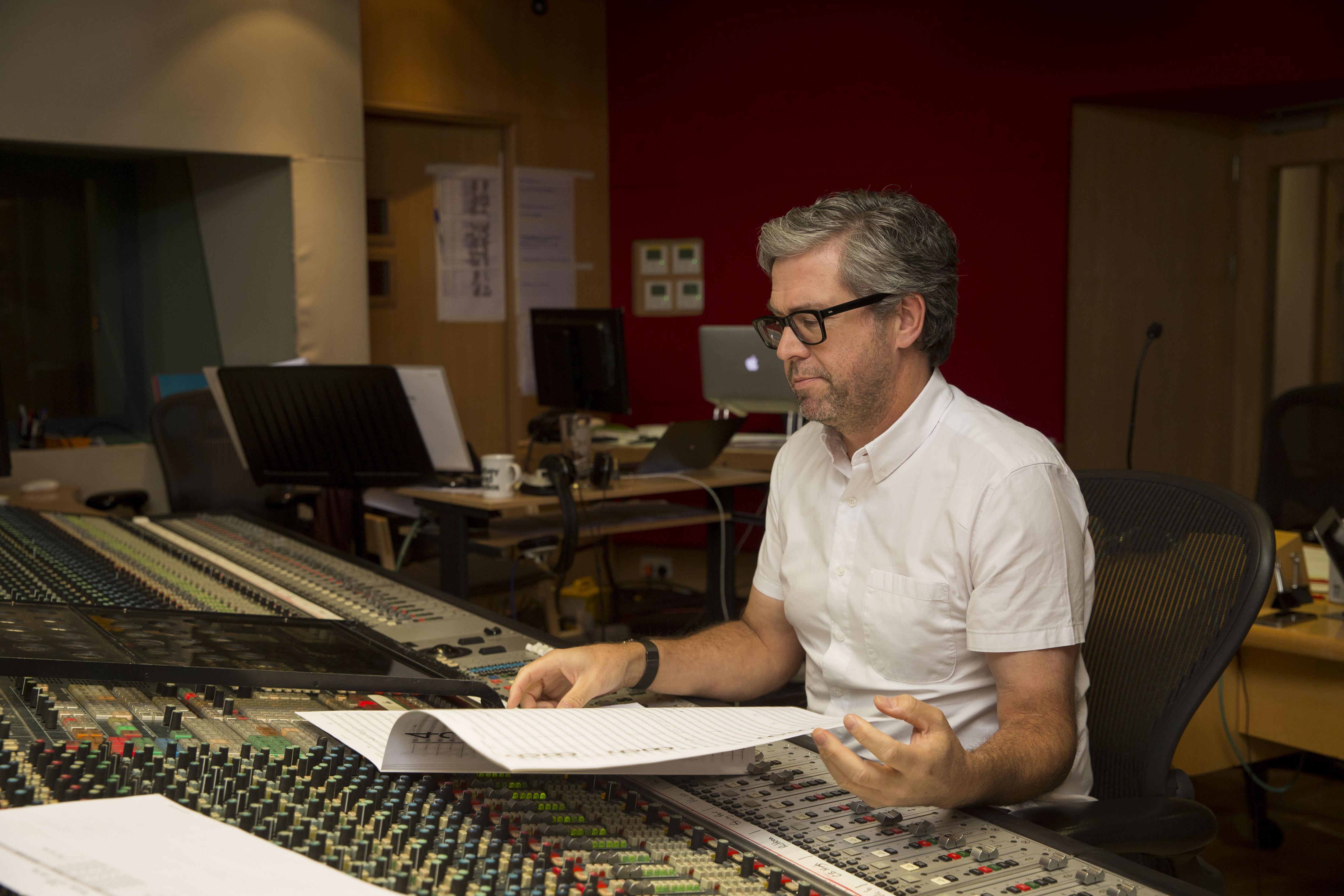 A man looking at some papers on a sound mixing board.