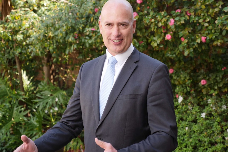 WA Opposition shadow treasurer Dean Nalder stands in a garden smiling wearing a suit with his hands outstretched.