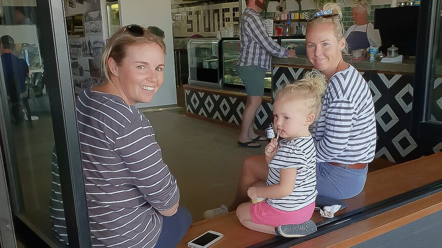 Two women and a child sit in the window of a cafe