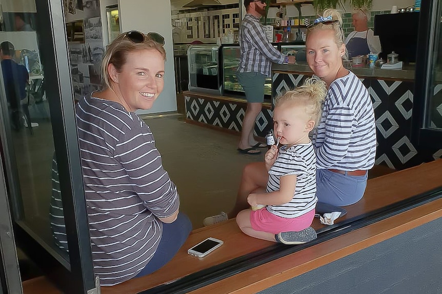 Two women and a child sit in the window of a cafe