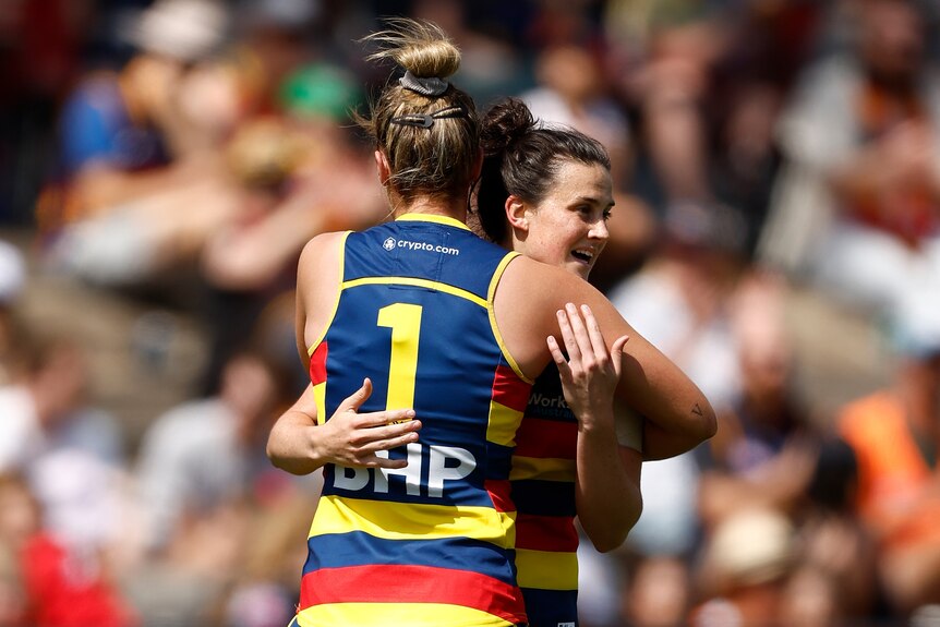 An Adelaide Crows AFLW player hugs her smiling teammate after a goal in a final.