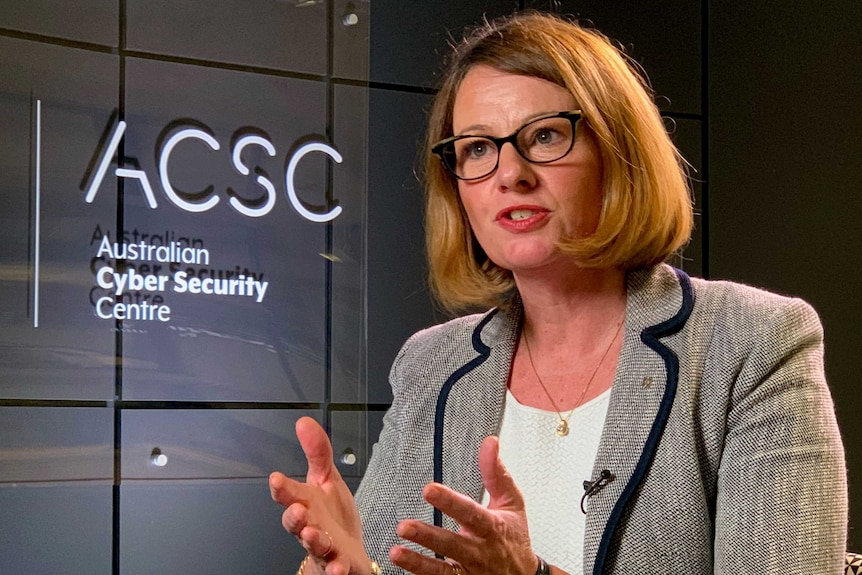 A woman sits in front of a sign for the Australian Cyber Security Centre.