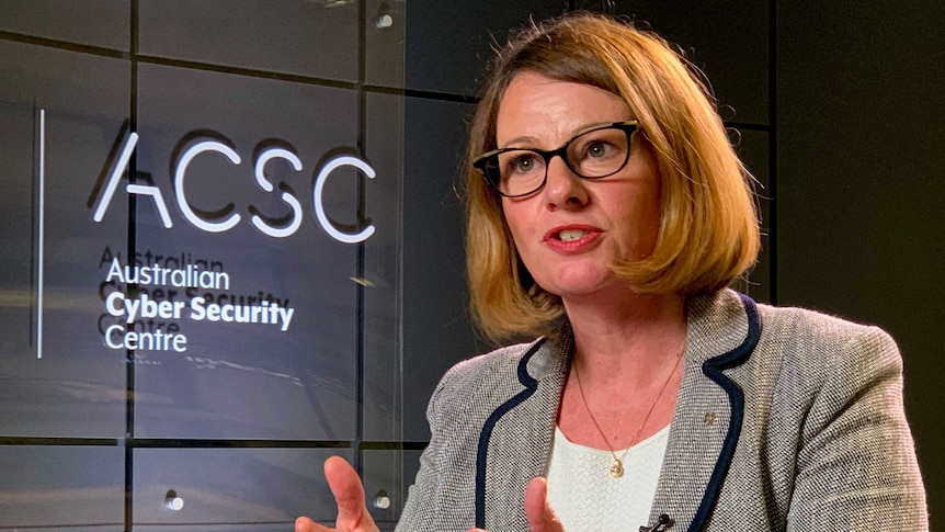 A woman sits in front of a sign for the Australian Cyber Security Centre.