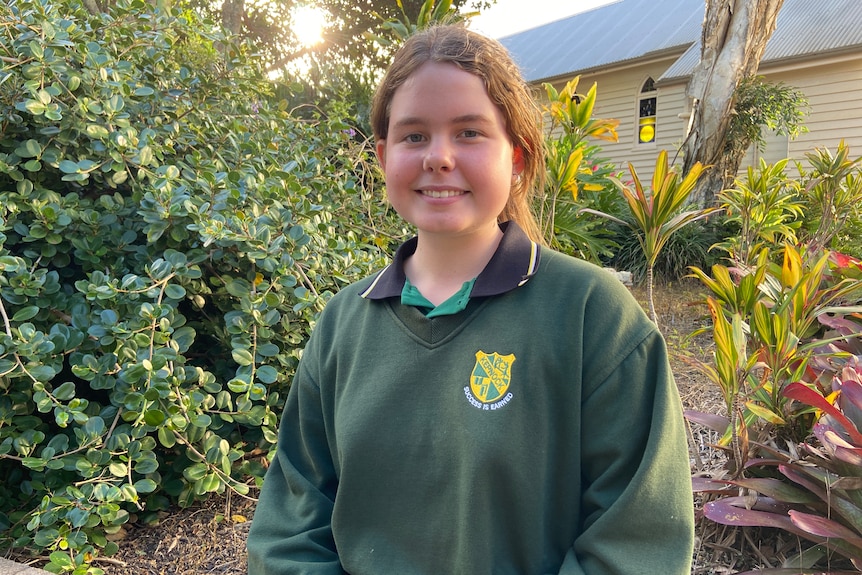 A smiling girl in a school jumper stands in a garden.