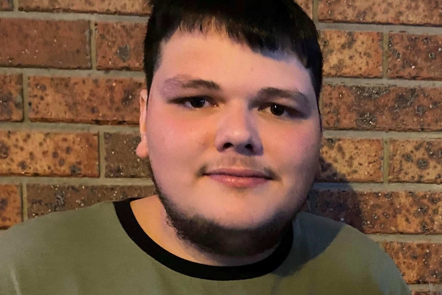 A young man in a Fila t-shirt stands in front of a brick wall.