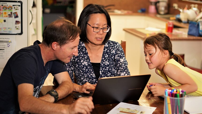 A family staring at a laptop at a kitchen table
