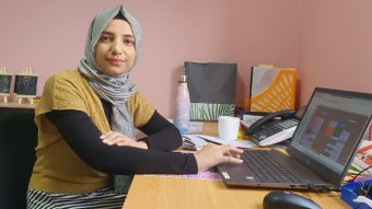 Annie Haider smiles at the camera as she sits at a laptop.