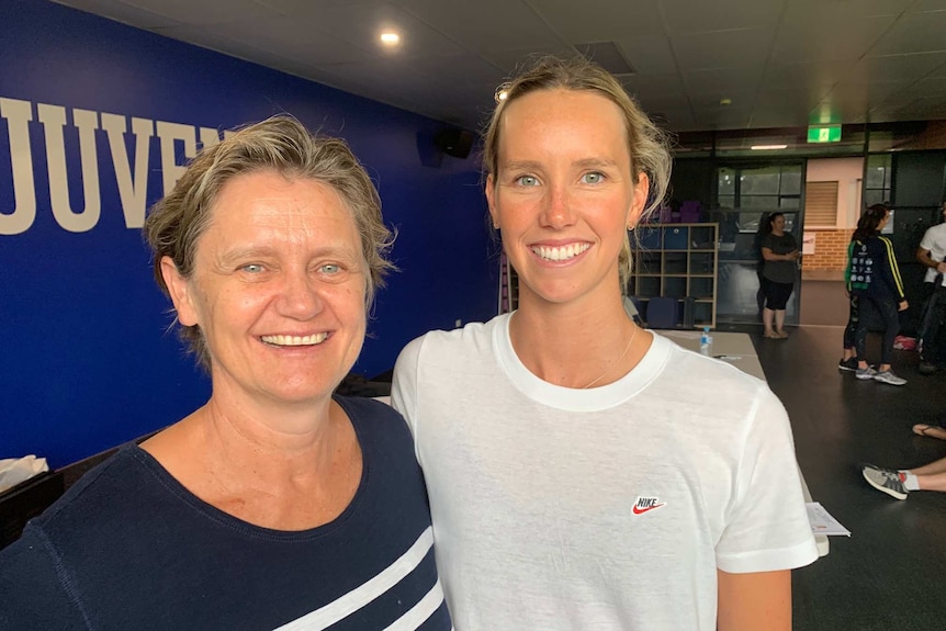 An older woman and a younger woman stand with their arms around one another, smiling.